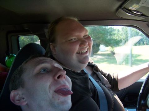 1985 Ford Bronco - Two individuals are inside a vehicle, with one person driving and smiling while the other playfully sticks out their tongue.