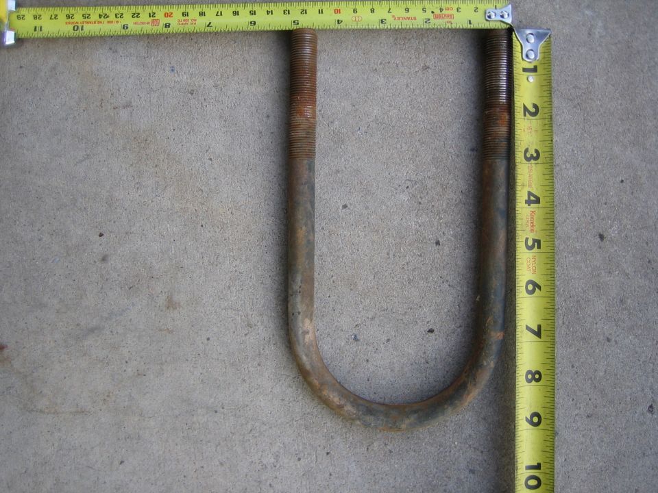 Rusty U-bolt on concrete measured with yellow Stanley tape measures