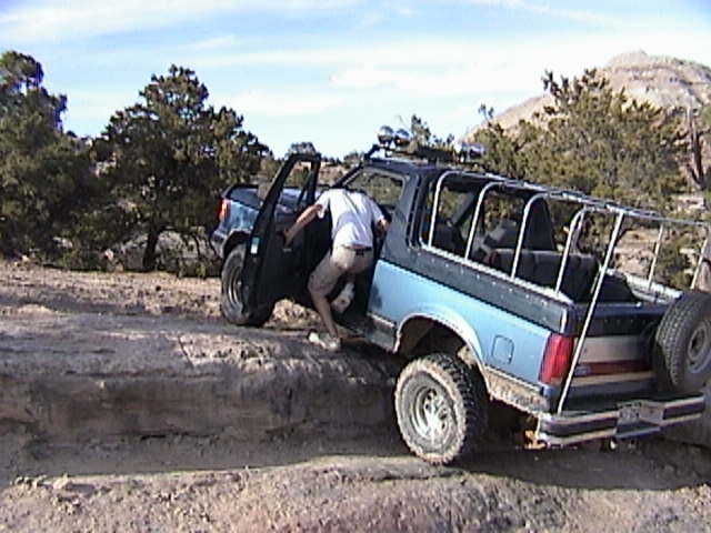 Blue Ford Bronco with roll cage on a rocky off-road trail, man stepping out