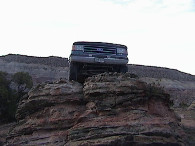 Front view of a 1990s Ford Bronco climbing over rocks