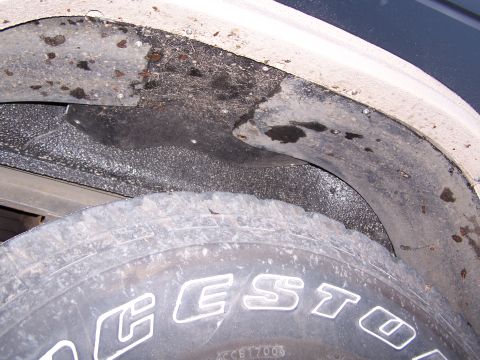 1986 Ford Bronco - A close-up view of a vehicle's wheel well liner and tire, showing dirt and wear.