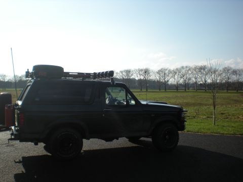 1993 Ford Bronco - Side view of a black Ford Bronco with a roof rack and spare tire, parked outdoors.