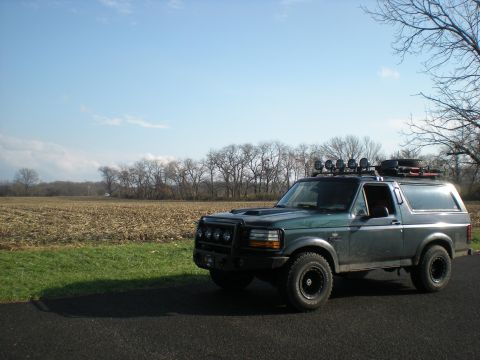 1993 Ford Bronco - This 1993 Ford Bronco is equipped with a roof rack and auxiliary lights, parked beside a harvested field under a clear blue sky.