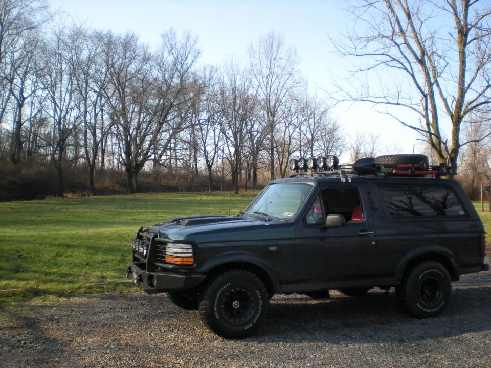 Dark green Ford Bronco with roof rack and off-road lights parked on a gravel road