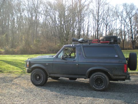 1993 Ford Bronco - This SUV, likely a Ford Bronco, is viewed from the side with a roof rack and spare tire, suggesting it is equipped for off-road use.