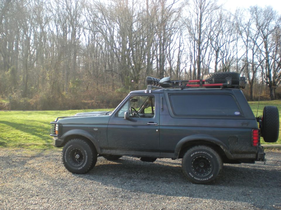 Dark gray SUV, possibly a Ford Bronco, with a roof rack carrying tools and a spare tire. It has aftermarket wheels and a spare tire mounted on the rear