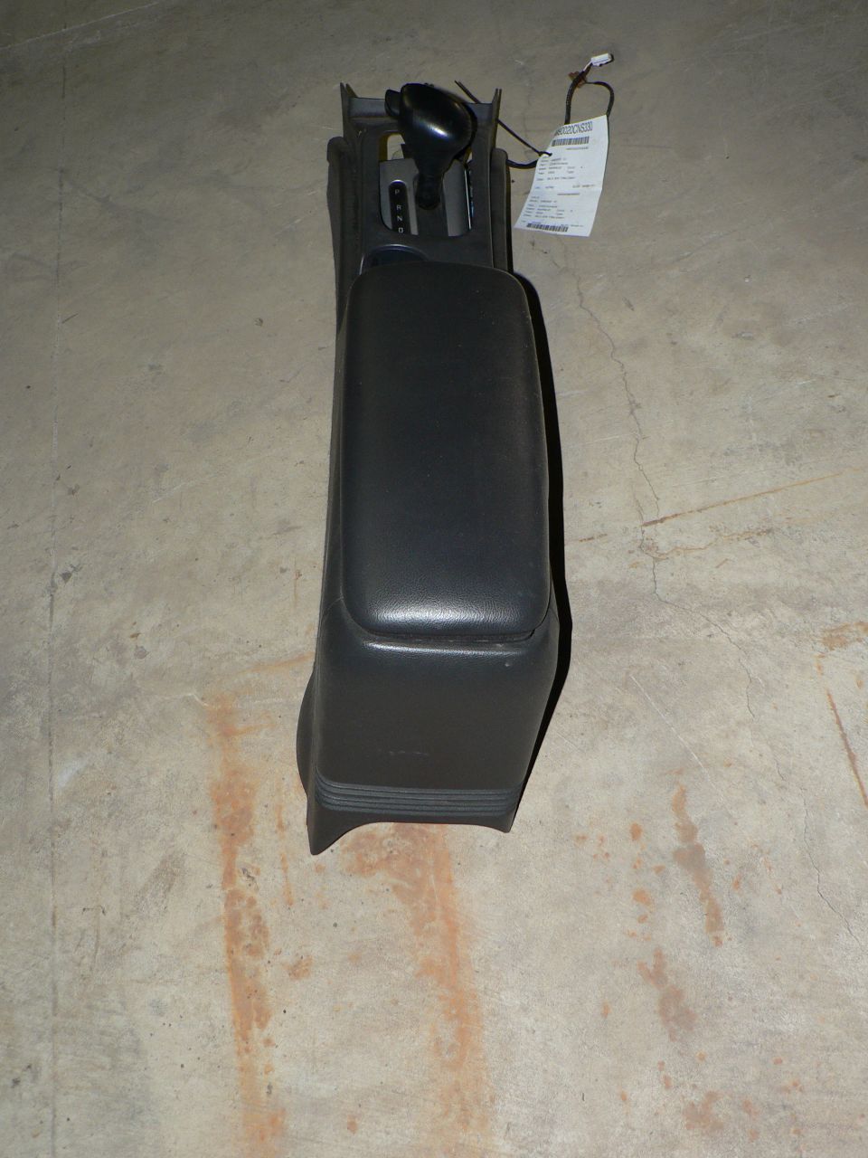 Gray center console with automatic floor shifter and salvage tag on concrete floor