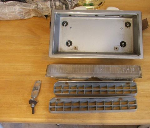 1989 Ford Bronco II - Various car parts are laid out on a wooden surface, including a license plate frame, taillight, grilles, and an emblem.