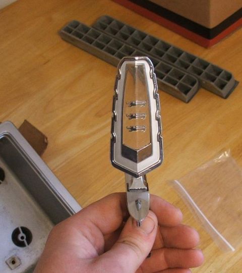 1989 Ford Bronco II - A car emblem is held in a hand, with other parts in the background.