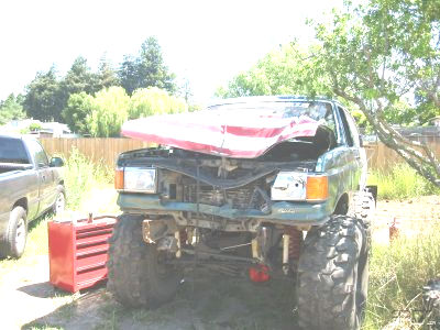 1994 Ford Bronco - This lifted 1994 Ford Bronco is green and has its hood open, parked next to a pickup truck.