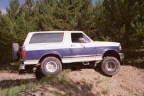 1994 Ford Bronco - This two-tone Ford Bronco is shown from a three-quarter front view, driving on an off-road trail.