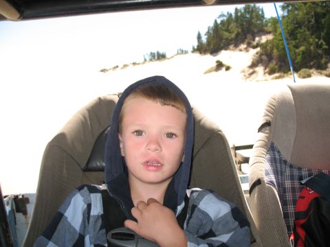 1976 Ford Bronco - A young boy is seated inside a vehicle, with a sandy landscape visible outside.