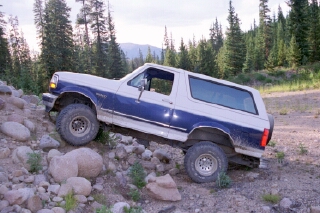 1994 Ford Bronco - This 1994 Ford Bronco is navigating a challenging rocky trail in a wooded area.