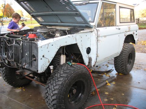 1976 Ford Bronco - A young boy inspects the engine bay of a classic Ford Bronco, which is parked outside with its hood raised.