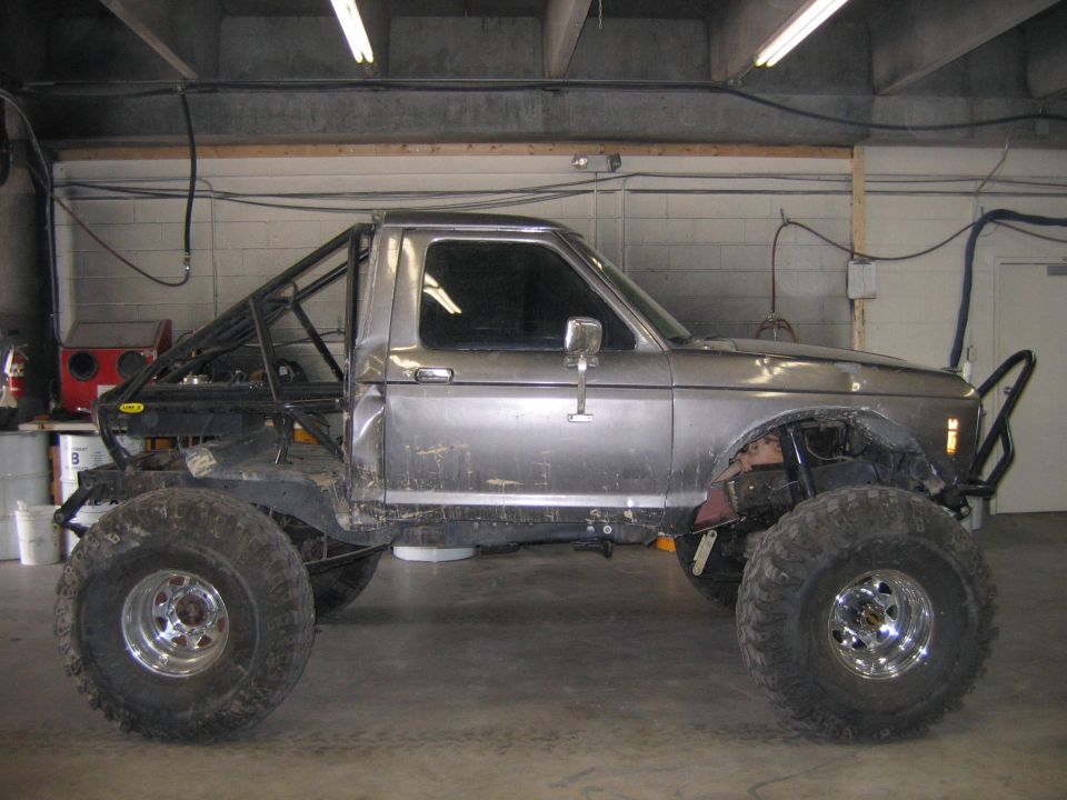 Modified pickup truck with large tires and roll cage, side view. Appears to be from the early 1980s