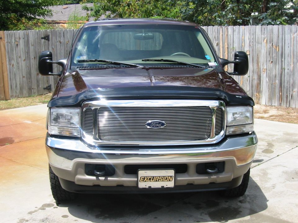 Front view of dark maroon Ford Excursion with chrome billet grille, hood deflector, and EXCURSION plate on driveway