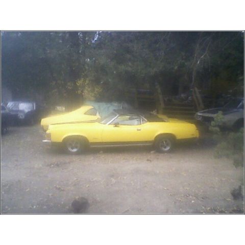 1973 Mercury Cougar - Side view of a yellow 1973 Mercury Cougar convertible parked outdoors.