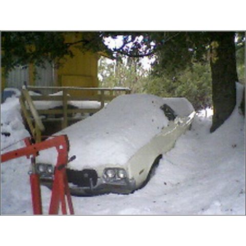 1972 Ford Ranchero - A vehicle sits partially buried in snow, with a red engine hoist positioned nearby.
