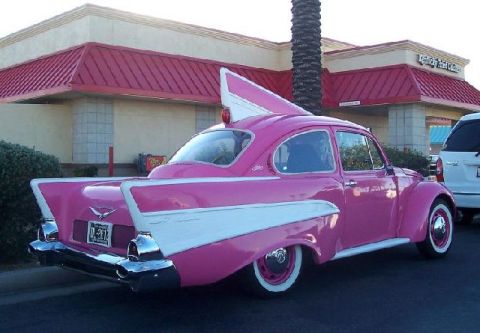 1991 Ford Crown Victoria - A custom pink car with prominent fins is parked outside a building.