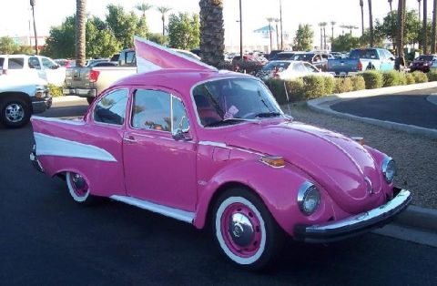 1991 Ford Crown Victoria - A customized pink Volkswagen Beetle with distinctive white fins and whitewall tires is parked outdoors.