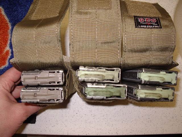 Tan tactical pouch holding six loaded magazines, with a hand inserting another
