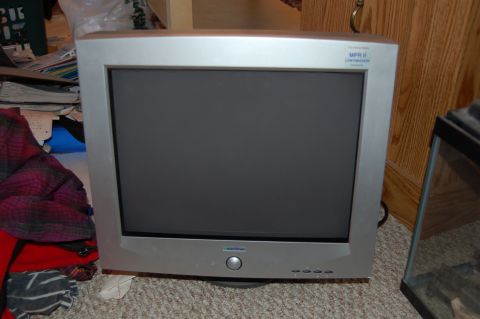 1991 Ford Probe - A silver CRT television is shown in a cluttered room, with a pile of clothes to its left and a glass tank to its right.