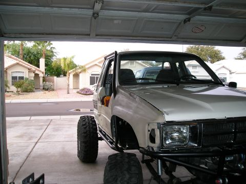 1986 Toyota Hilux - A modified white pickup truck with oversized tires sits in a garage, ready for off-road adventures.