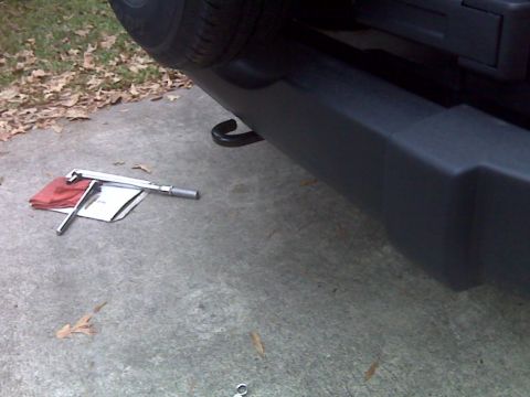 2008 Jeep Wrangler - A close-up view of a vehicle's rear bumper and spare tire, with a jack and tools laid out on the ground nearby.