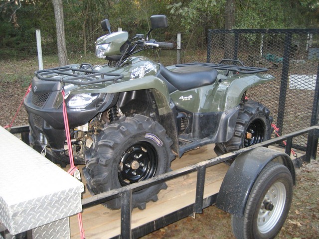 Green Suzuki King Quad 4x4 ATV strapped onto a utility trailer outdoors