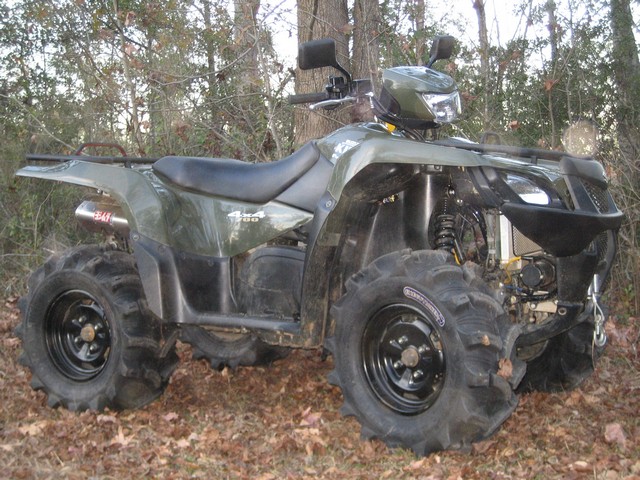 Green Suzuki King Quad 4x4 700 ATV parked in woods with mud tires