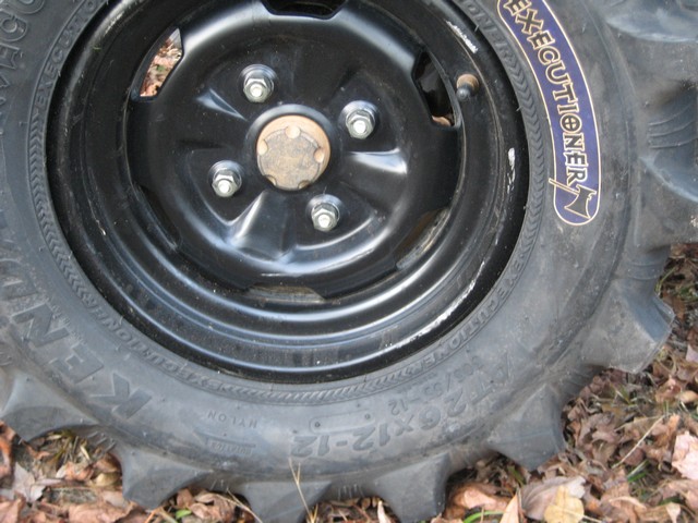 Black steel ATV wheel with Kenda 22x12-12 Executioner tire on leafy ground