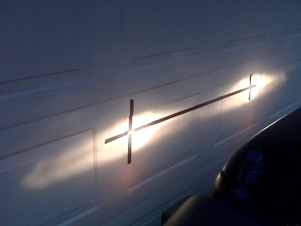 Metal cross-shaped object against a white garage door at sunset