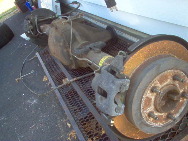 Rear axle assembly with rusty brake rotors and calipers, viewed from the side