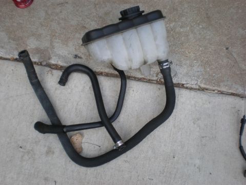 2007 Ford Mustang - A detached coolant reservoir and hoses are shown on a concrete surface.