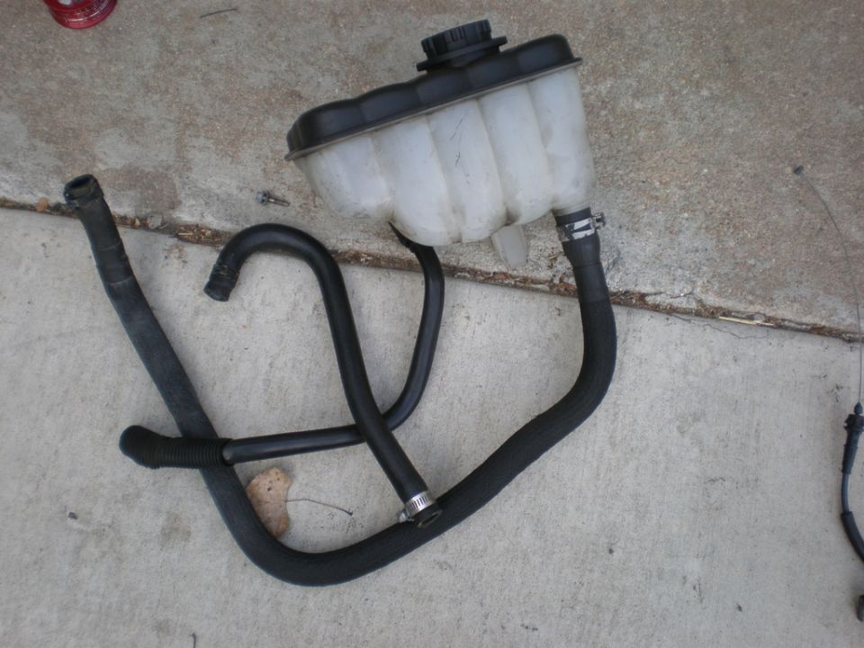 Coolant reservoir with hoses attached, lying on concrete