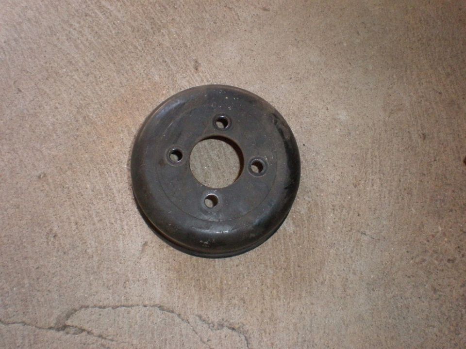 Round metal pulley with three bolt holes around a central opening, resting on concrete