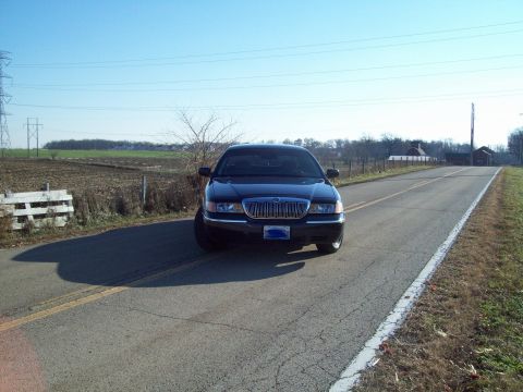 1999 Mercury Grand Marquis - A dark 1999 Mercury Grand Marquis is seen from the front on a two-lane road with fields in the background.