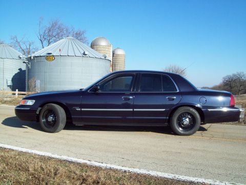 1999 Mercury Grand Marquis - Side view of a dark blue sedan with black steel wheels parked on a rural road.