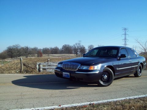 1999 Mercury Grand Marquis - A dark sedan is parked on the side of a road with a rural landscape behind it.