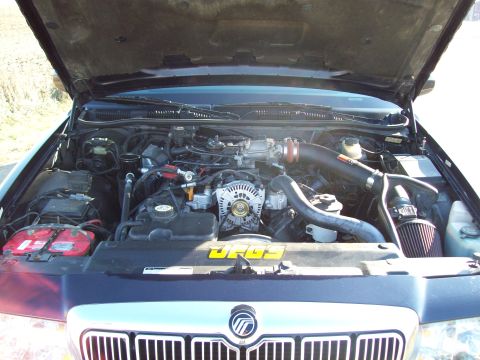 1999 Mercury Grand Marquis - The engine bay of a 1999 Mercury Grand Marquis is visible with the hood raised, revealing the V8 engine components.