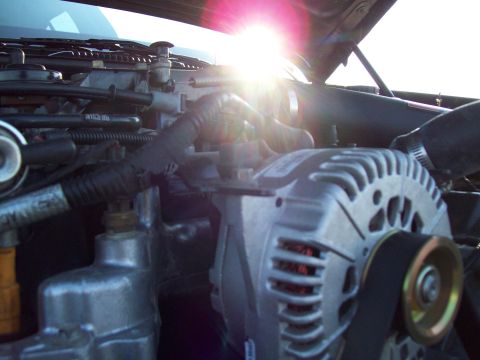 1999 Mercury Grand Marquis - Close-up of a vehicle's engine bay, focusing on the alternator with sunlight shining through.