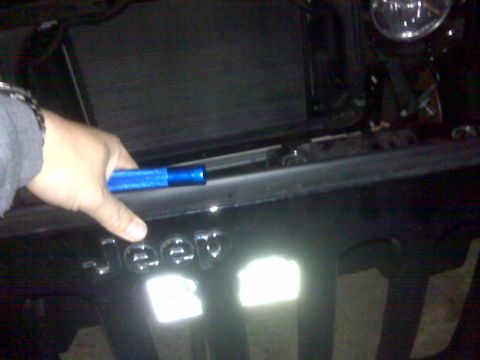 2008 Jeep Wrangler - Hand holding a blue tool near the Jeep grille badge on a 2008 Jeep Wrangler.