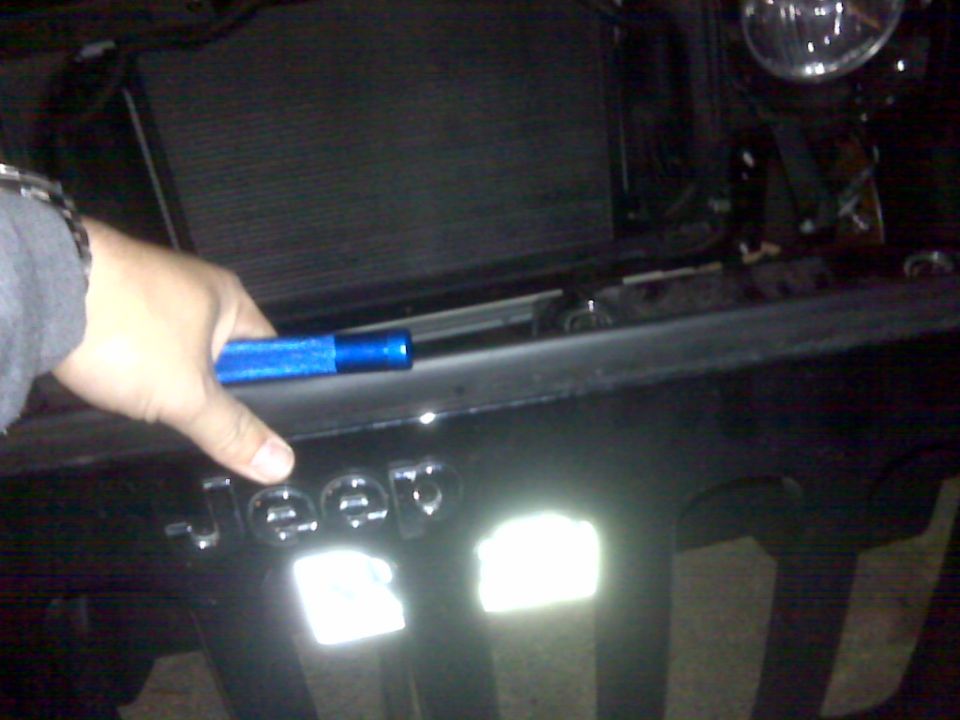 Hand holding blue tool near Jeep grille badge. 2008 Jeep Wrangler