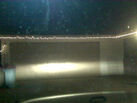 2008 Jeep Wrangler - Headlights cast a bright beam onto a closed garage door, with decorative lights strung across the top of the structure.