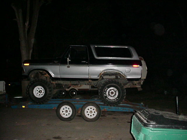 Lifted black and silver Ford Bronco on a car trailer at night, side view