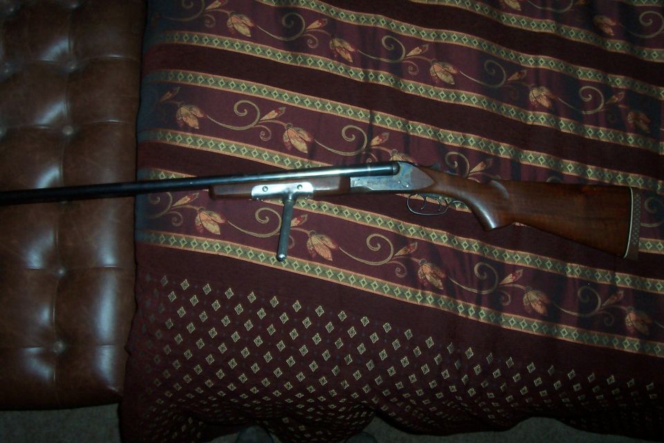 Double-barreled shotgun with wooden stock and metal barrel, lying on a patterned fabric
