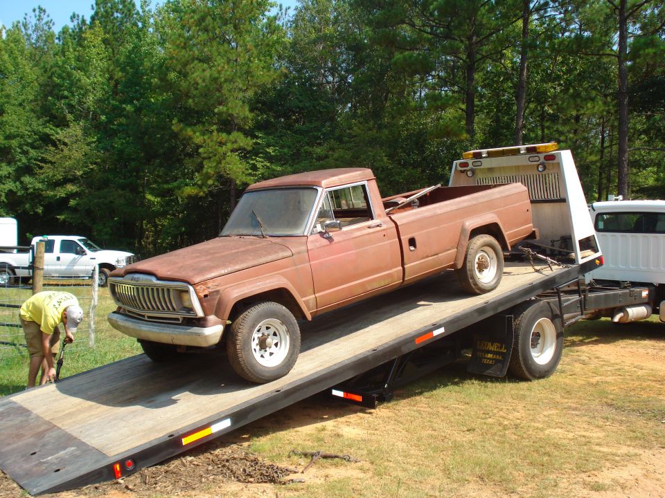 Rusty brown 1980s Jeep pickup truck being loaded onto a flatbed tow truck