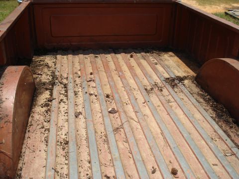 1984 Jeep J-10 - The bed of a pickup truck shows wear and tear with dirt and debris scattered across the wooden floor.