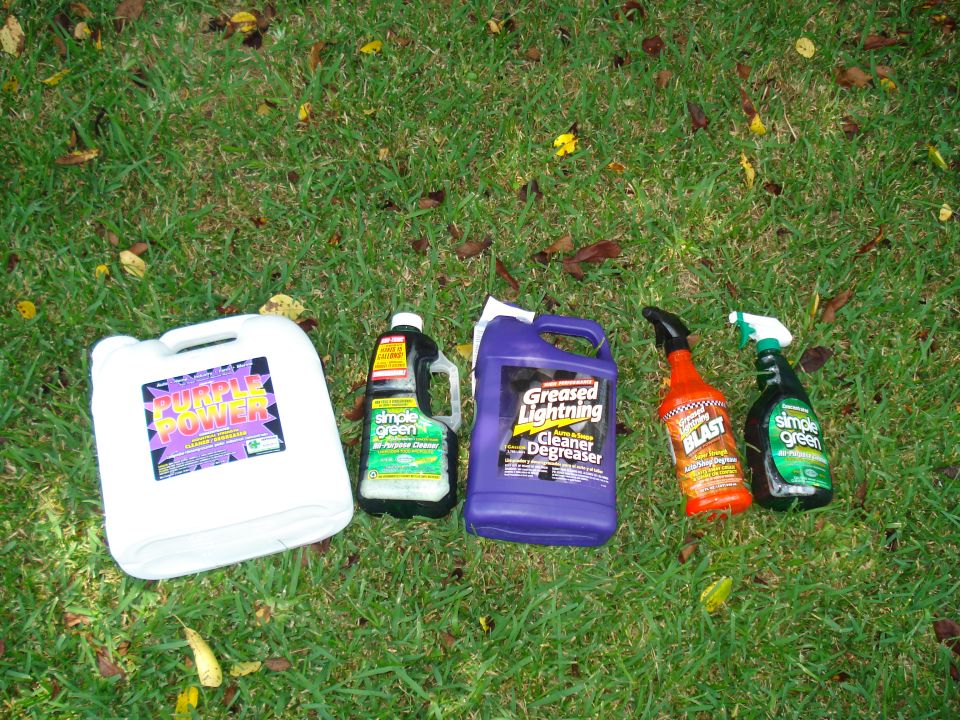 Five bottles of cleaning products on grass: Purple Power, Simple Green, Greased Lightning, and two more