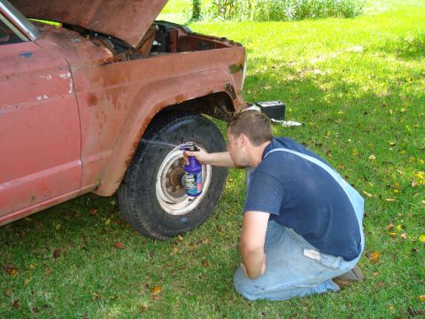1984 Jeep J-10 - A man sprays the tire of a rusty red 1984 Jeep J-10 pickup truck.